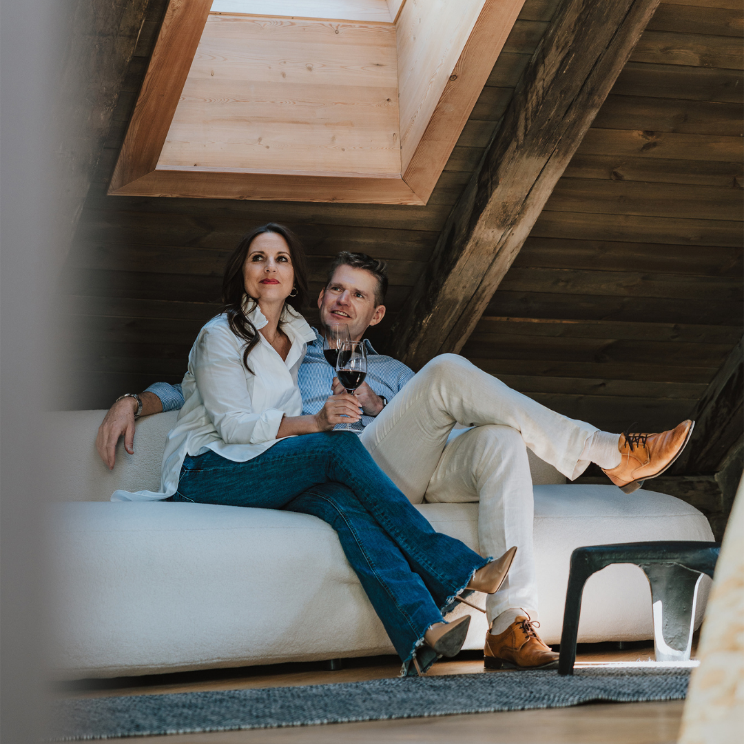 Paar entspannt bei einem Glas Wein in einem gemütlichen Innsbruck Hotel Zimmer mit Dachfenster.